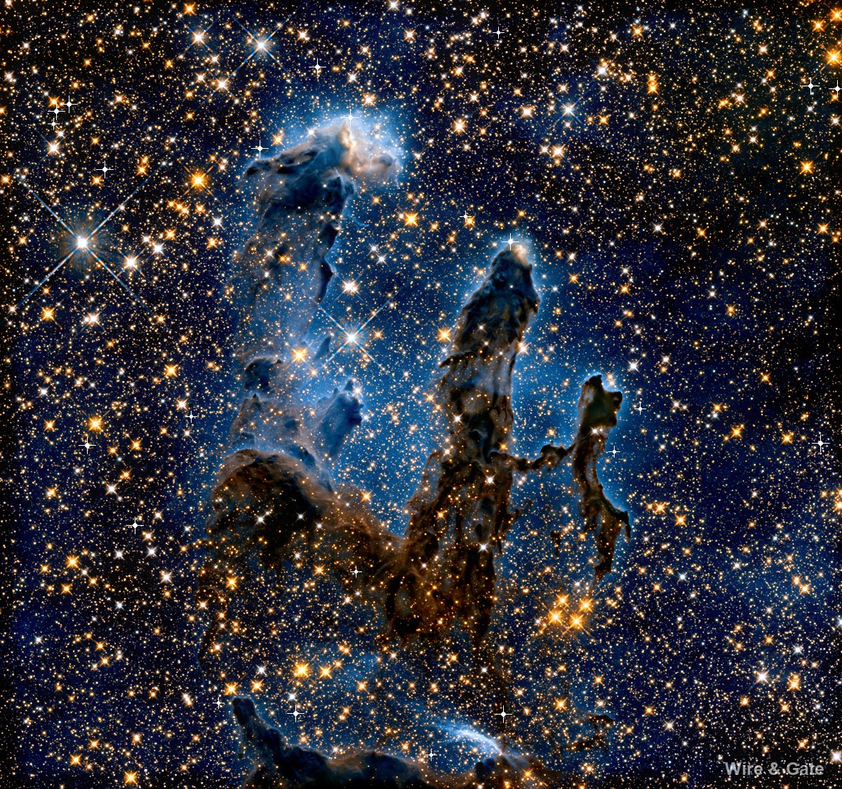 Three columns of dark gas with bluish edges, rising through a field of orange stars
